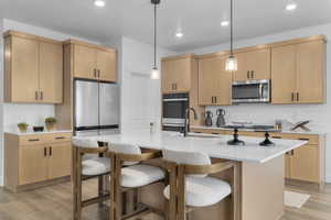 Kitchen featuring light wood finish cabinetry, light stone counters, hanging light fixtures, and light wood-type flooring