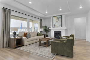 Living area featuring light wood finished floors, a glass covered fireplace, a tray ceiling, and recessed lighting