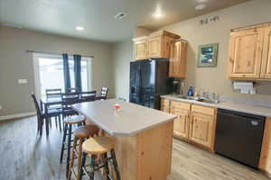 Kitchen featuring light wood finish cabinets, black appliances, light countertops, a center island, and light wood-style flooring