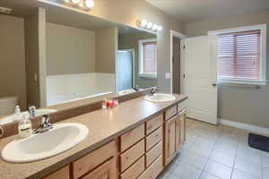 Bathroom with double vanity, light tile patterned floors, a garden tub, and healthy amount of natural light