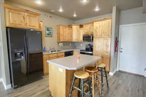 Kitchen featuring light wood finish cabinetry, black appliances, light countertops, a kitchen breakfast bar, and a center island