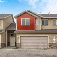 View of front of house featuring stone siding, roof with shingles, asphalt driveway, an attached garage, and board and batten siding