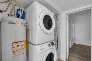 Laundry area with electric water heater, stacked washing machine and dryer, and wood finished floors