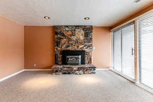Unfurnished living room featuring carpet, a fireplace, a textured ceiling, and recessed lighting