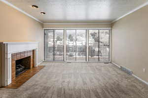 Unfurnished living room featuring carpet, a textured ceiling, a fireplace, and ornamental molding