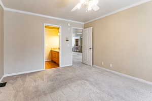 Unfurnished bedroom featuring light carpet, ornamental molding, a ceiling fan, and ensuite bath