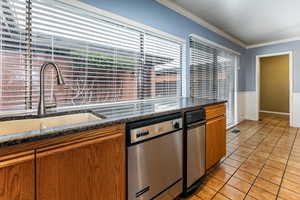Kitchen featuring wood finish cabinets, wainscoting, dishwasher, crown molding, and dark stone counters