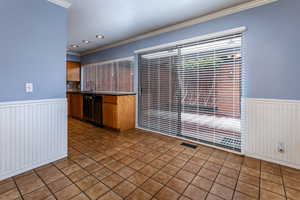 Kitchen featuring a wainscoted wall, crown molding, wood finish cabinets, dark tile patterned floors, and black dishwasher