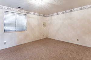 Spare room featuring a textured ceiling, carpet floors, electric panel, and wallpapered walls