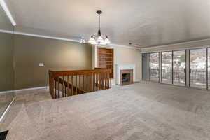 Unfurnished living room with a textured ceiling, carpet, a fireplace, ornamental molding, and hanging lights