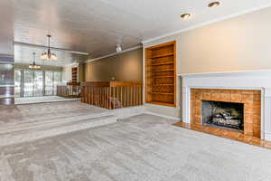 Unfurnished living room with built in shelves, a textured ceiling, a chandelier, carpet floors, and crown molding