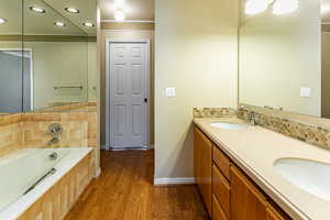Full bathroom featuring recessed lighting, double vanity, a bath, dark wood-type flooring, and ornamental molding