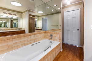 Full bath with ornamental molding, a garden tub, and dark wood finished floors