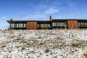 Snow covered back of property with a chimney and brick siding