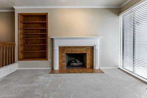 Unfurnished living room with built in features, crown molding, carpet flooring, a tiled fireplace, and a textured ceiling