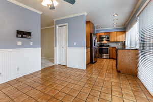 Kitchen with wood finish cabinets, crown molding, stainless steel appliances, a ceiling fan, and light tile patterned floors
