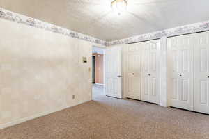 Unfurnished bedroom with a textured ceiling, two closets, carpet flooring, and wallpapered walls