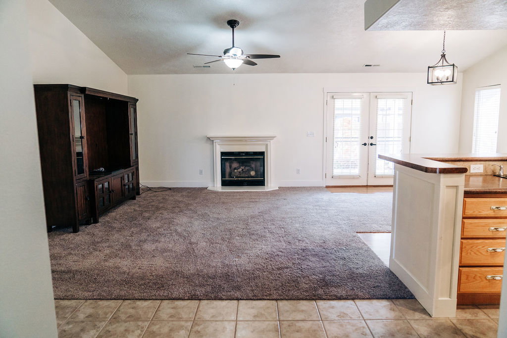 Unfurnished living room featuring vaulted ceiling, light carpet, ceiling fan, french doors, and a glass covered fireplace