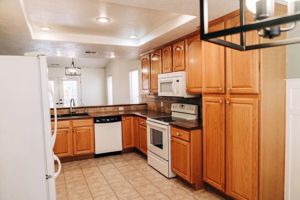 Kitchen with white appliances, dark countertops, a tray ceiling, wood finish cabinets, and a chandelier