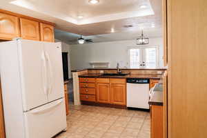 Kitchen featuring white appliances, a tray ceiling, dark countertops, a ceiling fan, and a peninsula