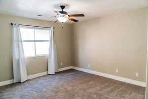 Carpeted spare room featuring ceiling fan and baseboards