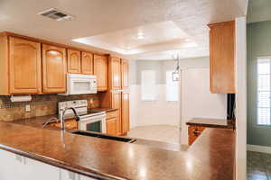 Kitchen with white appliances, a raised ceiling, dark countertops, a textured ceiling, and hanging light fixtures