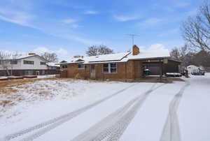 Snow covered house with a chimney, brick siding, a patio area, and roof mounted solar panels