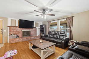 Living room featuring light wood finished floors, a ceiling fan, and a fireplace