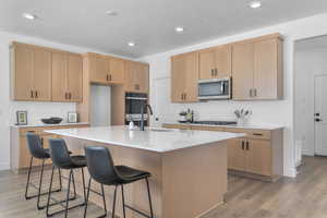 Kitchen with light wood-style flooring, a breakfast bar, a kitchen island with sink, light wood finish cabinets, and stainless steel appliances