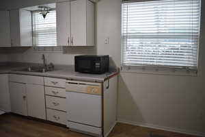 Kitchen featuring white cabinetry, white dishwasher, black microwave, light countertops, and wood finished floors