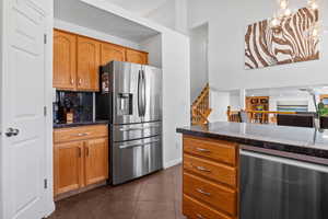 Kitchen featuring stainless steel appliances, dark tile patterned floors, a chandelier, wood finish cabinetry, and backsplash