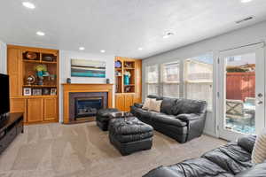 Living room with light colored carpet, built in shelves, a tiled fireplace, recessed lighting, and a textured ceiling