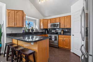 Kitchen featuring stainless steel appliances, a kitchen bar, a peninsula, wood finish cabinetry, and decorative backsplash