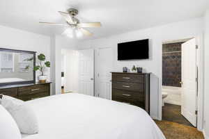 Bedroom with a ceiling fan, connected bathroom, and dark carpet