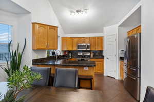 Kitchen featuring stainless steel appliances, a peninsula, decorative backsplash, wood finish cabinets, and vaulted ceiling