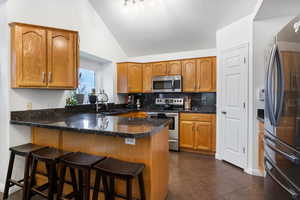 Kitchen featuring a peninsula, wood finish cabinets, stainless steel appliances, backsplash, and a kitchen breakfast bar