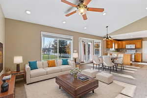 Living room featuring light carpet, a ceiling fan, a chandelier, and vaulted ceiling