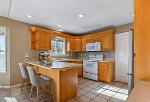 Kitchen with light countertops, white appliances, a peninsula, a breakfast bar, and light tile patterned floors