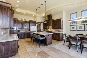 Kitchen featuring dark wood finish cabinets, a breakfast bar, an island with sink, decorative backsplash, and stainless steel microwave