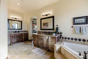 Bathroom featuring two vanities, a bath, stone tile flooring, and recessed lighting
