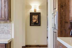 Kitchen with tasteful backsplash, stainless steel microwave, light stone counters, and wood finish cabinets