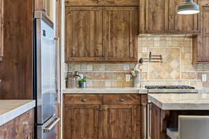 Kitchen featuring stainless steel appliances, wood finish cabinetry, backsplash, and light stone counters