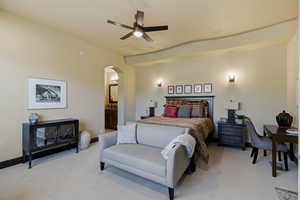 Carpeted bedroom with arched walkways, ceiling fan, and connected bathroom
