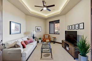 Living area featuring a ceiling fan, light colored carpet, and a tray ceiling