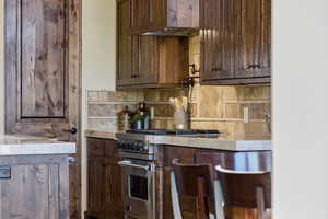 Kitchen featuring premium range, light stone counters, dark wood finish cabinetry, and backsplash