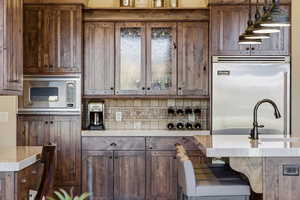 Kitchen featuring built in appliances, light stone countertops, a breakfast bar area, and dark wood finish cabinetry