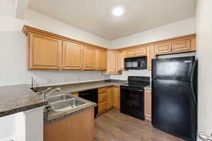 Kitchen with black appliances, dark countertops, dark wood-type flooring, and a peninsula