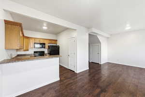 Kitchen with dark wood-style floors, black appliances, a peninsula, dark stone countertops, and open floor plan