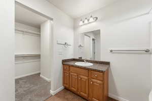 Master Bathroom featuring vanity, a walk in closet, dark colored carpet, and dark tile patterned floors