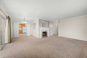 Unfurnished living room with suspended lighting, light carpet, a tile fireplace, and ornamental molding